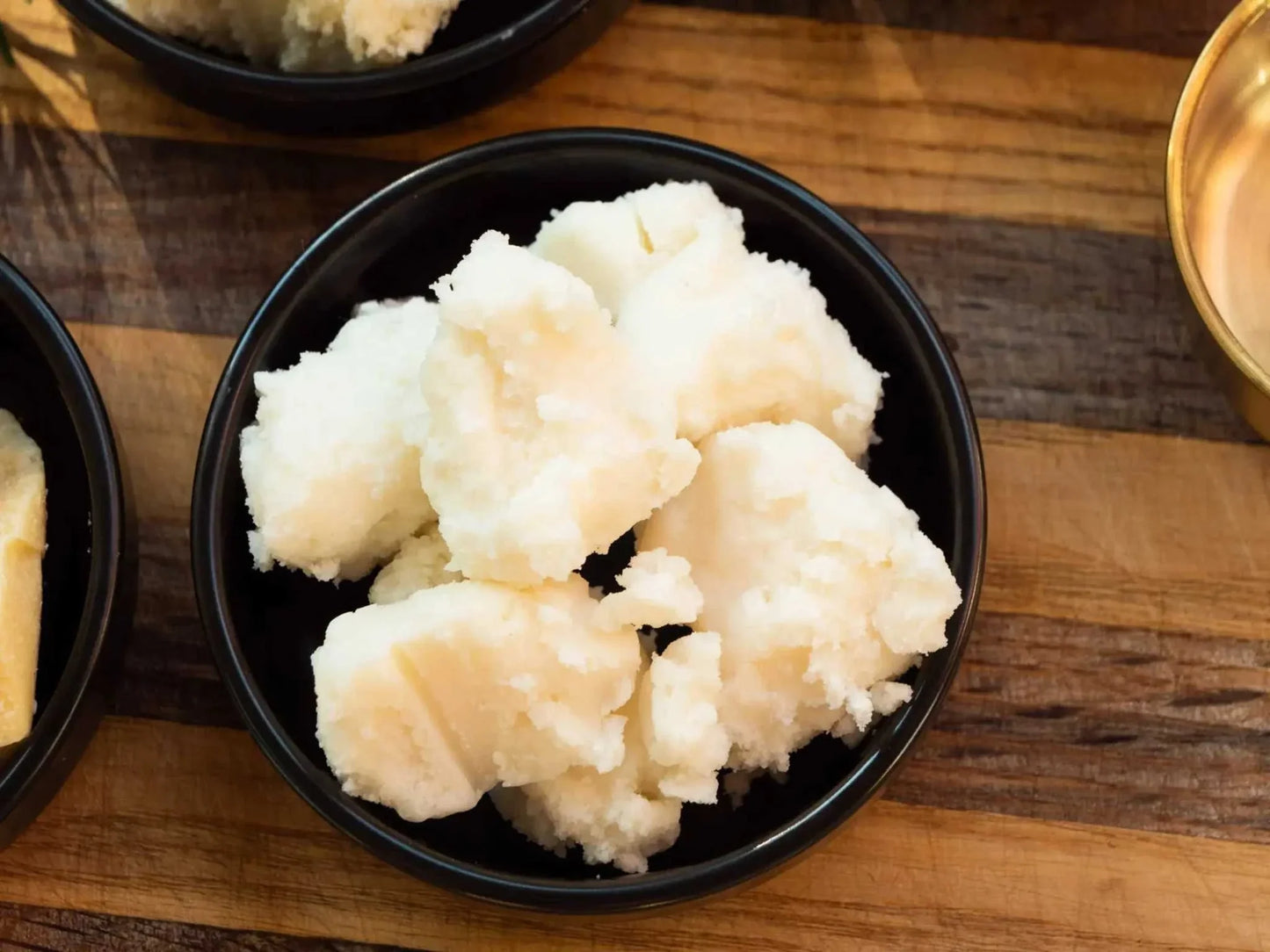 bulk pure mango butter in white chunks in black bowl on wooden surface for skincare use