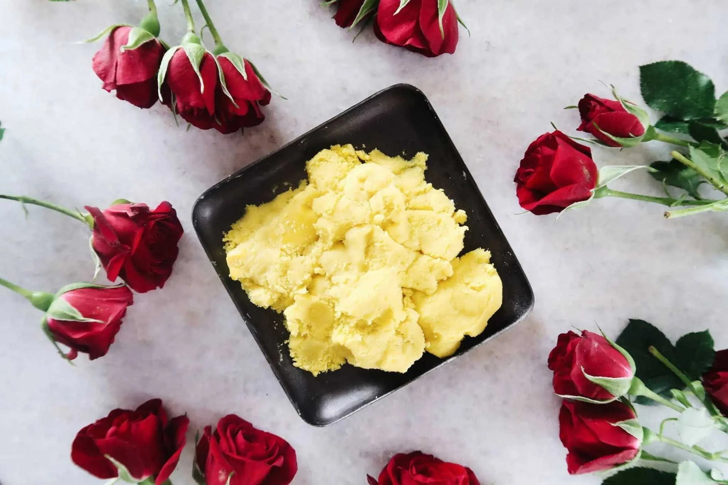 Yellow African Shea Butter in black bowl surrounded by red roses.