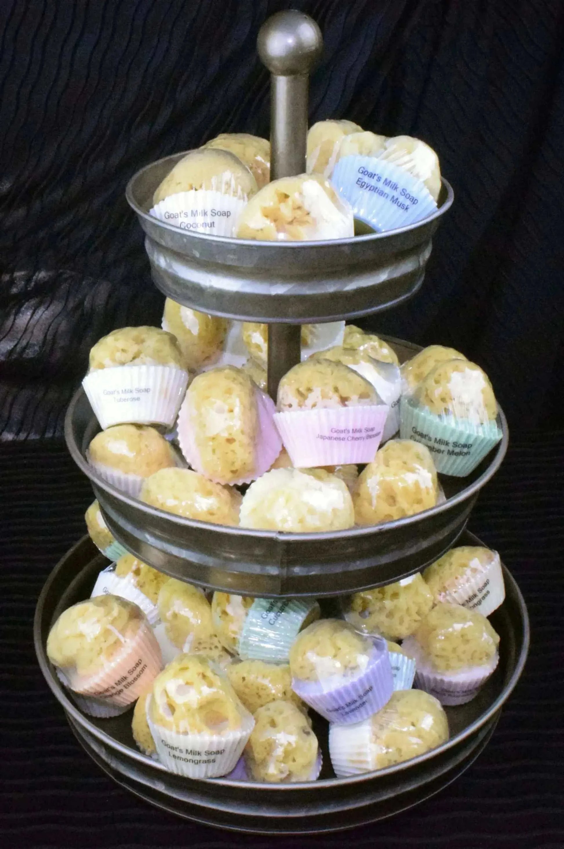 Three-tier galvanized steel cupcake display with goats milk and olive oil soaps embedded with natural sea sponges in pastel wrappers
