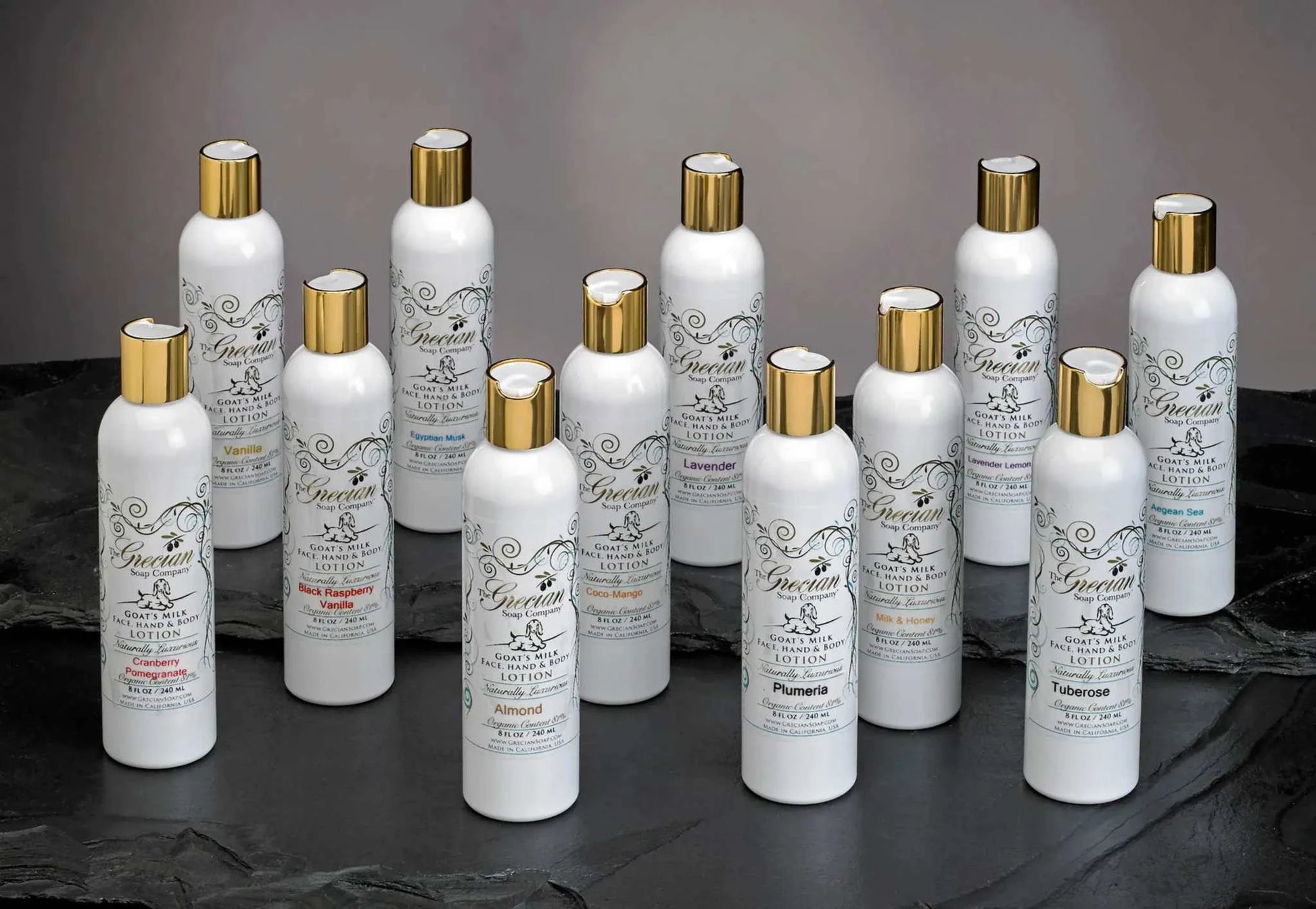 Array of Organic Goat's Milk Lotion bottles with gold caps from the Grecian Soap Company, showcasing various scents and rich, hydrating formulas.
