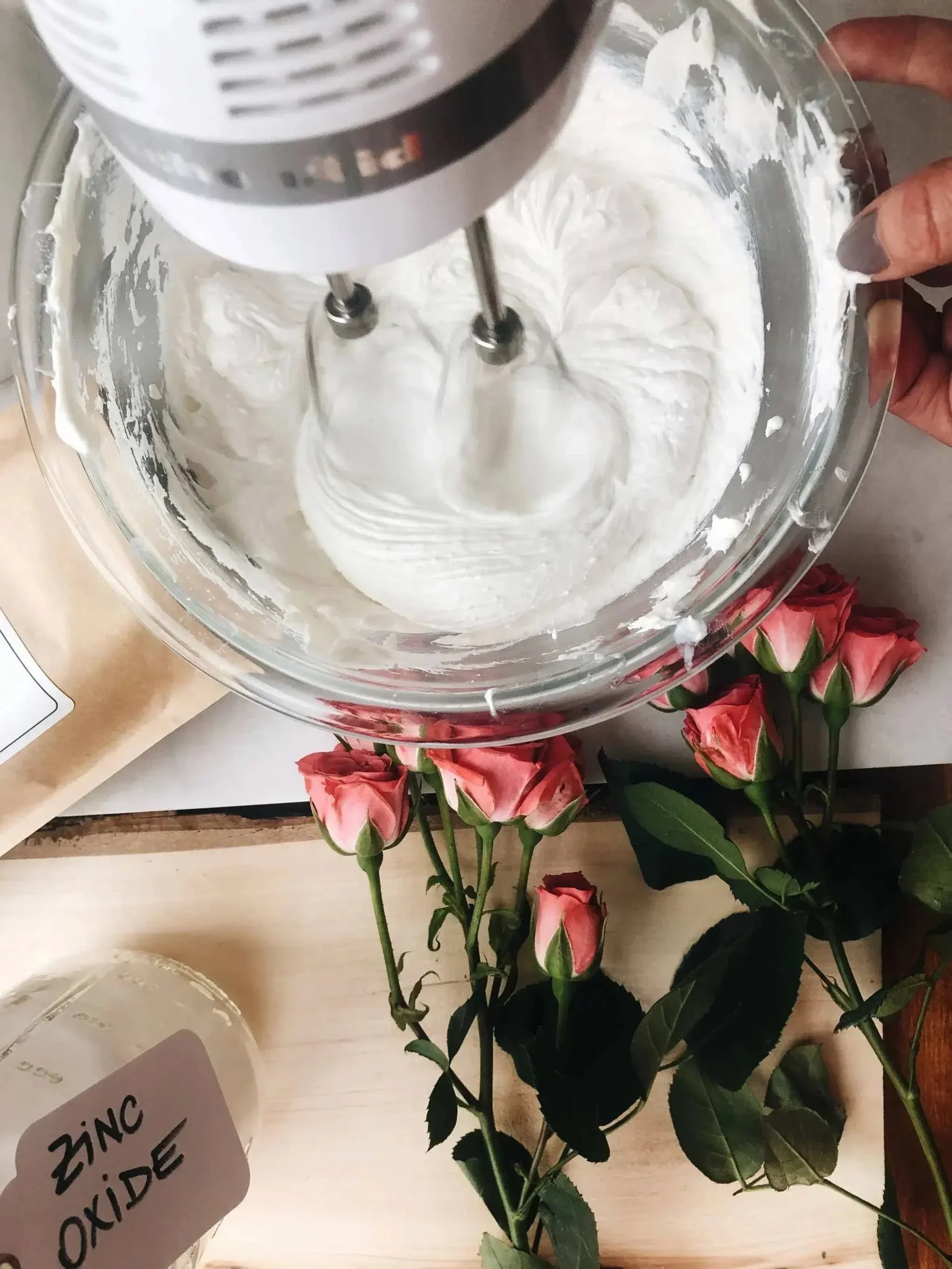 Mixing bulk shea butter with zinc oxide in a bowl for DIY skincare products with fresh roses nearby