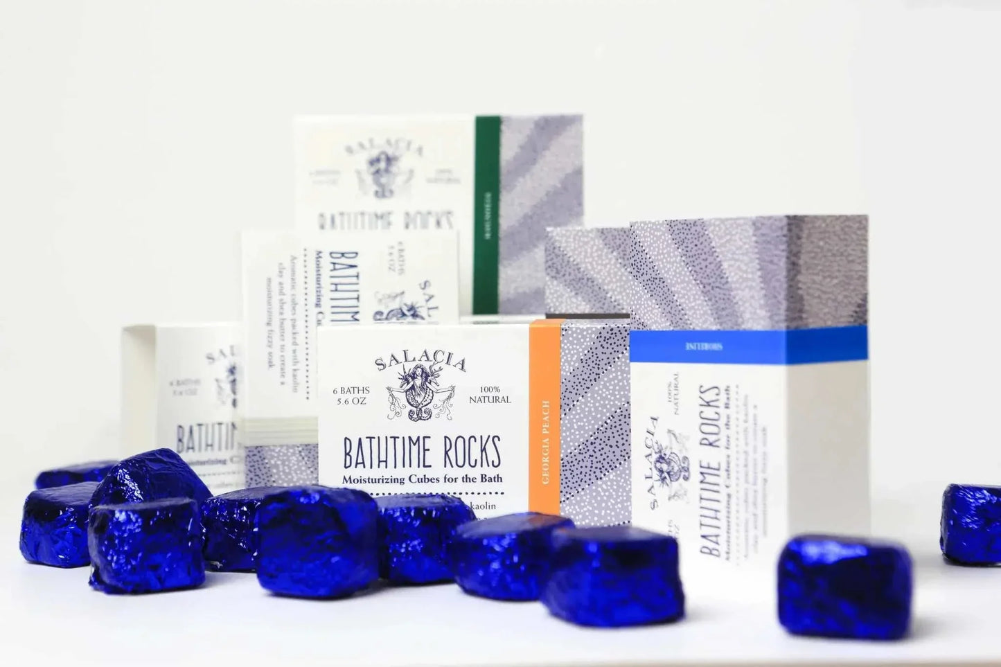 BathTime Rocks moisturizing bath cubes in blue foil with assorted scented packaging boxes in background