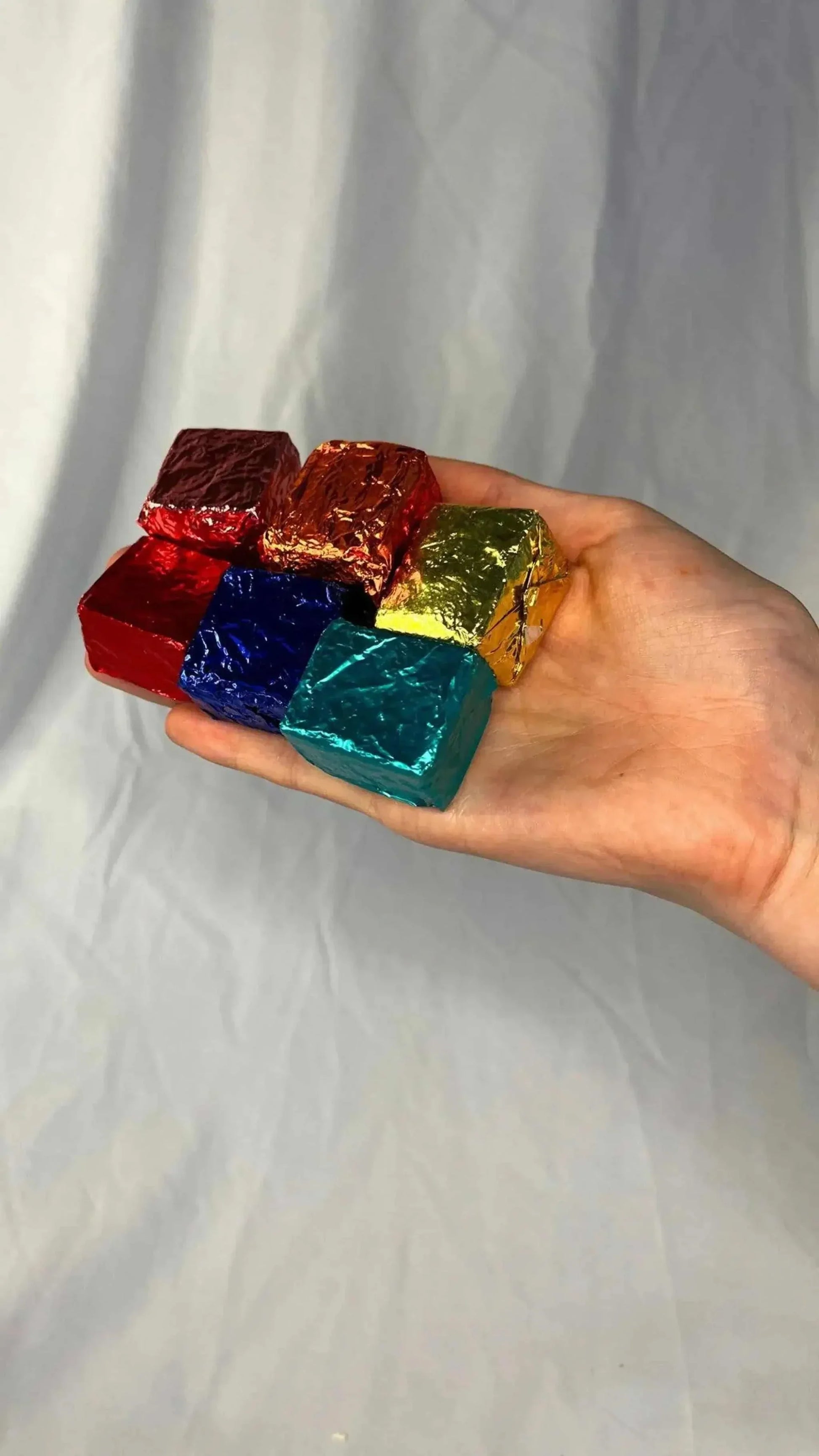 Hand holding six colorful foil-wrapped BathTime Rocks aromatic bath cubes in assorted scents