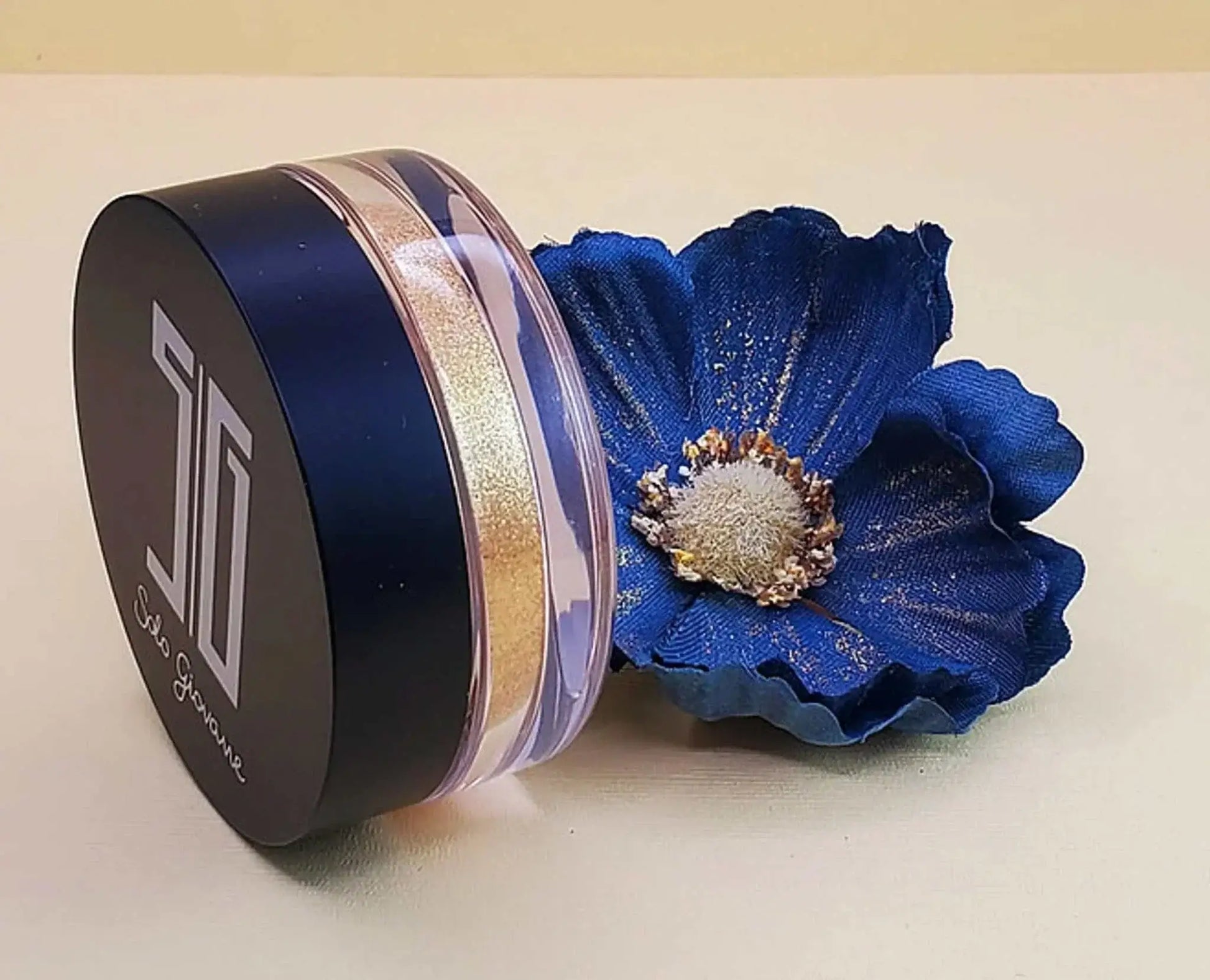 High pigment shimmering highlighting powder in container with blue flower.