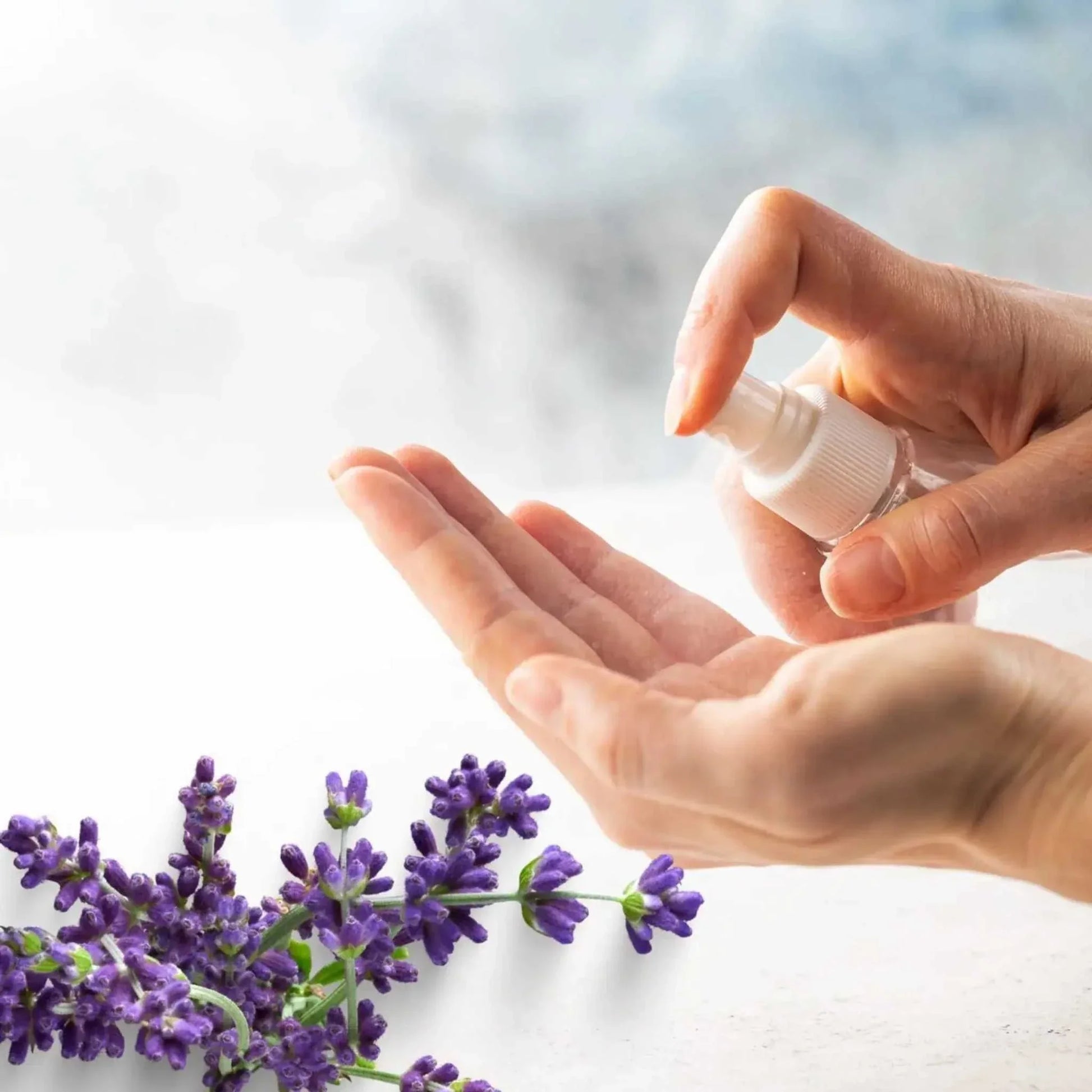 Hand using travel size sanitizing spray with lavender flowers nearby, showcasing moisturizing sanitizing spray product