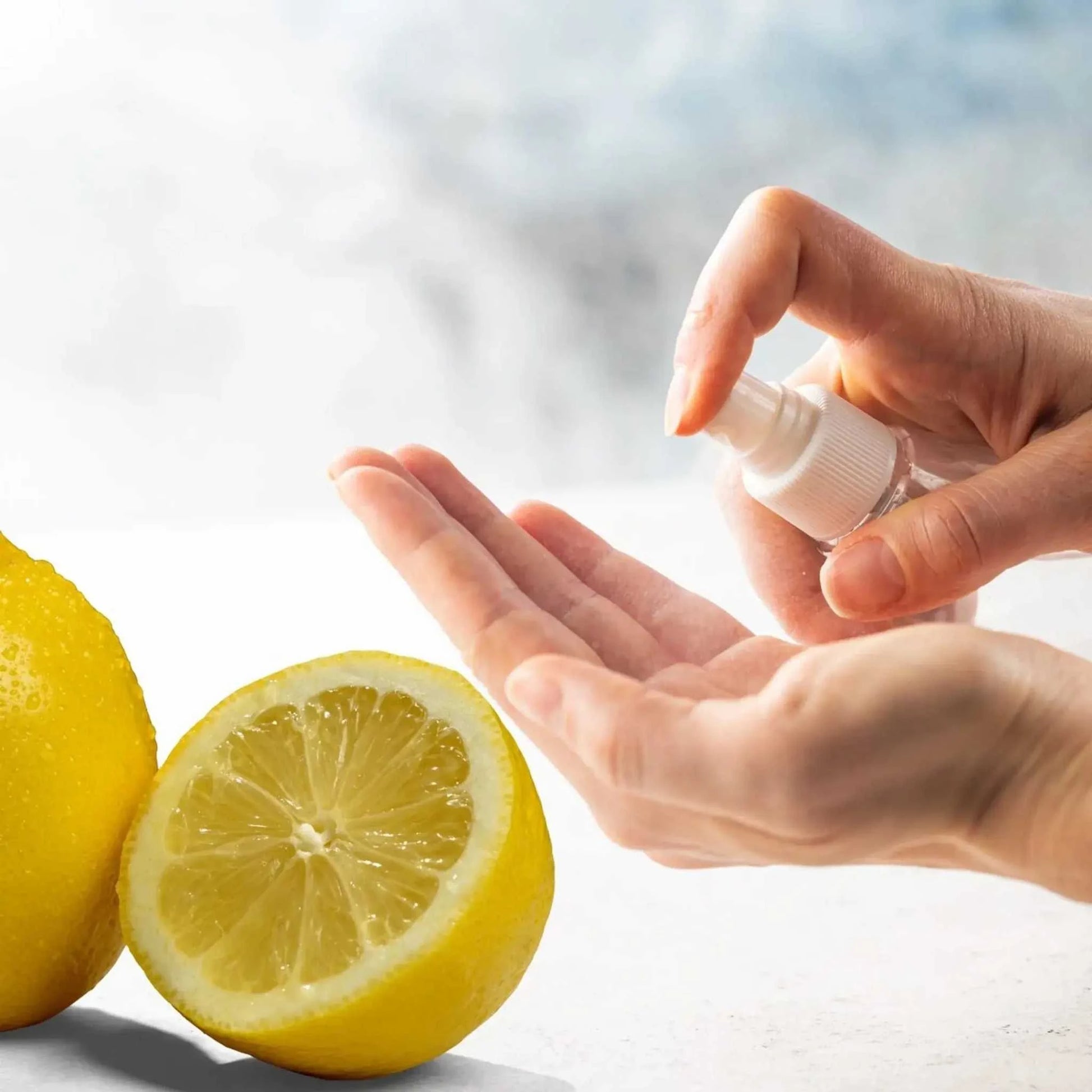 Hand spraying lemon-scented sanitizing spray on palm with fresh lemon halves nearby